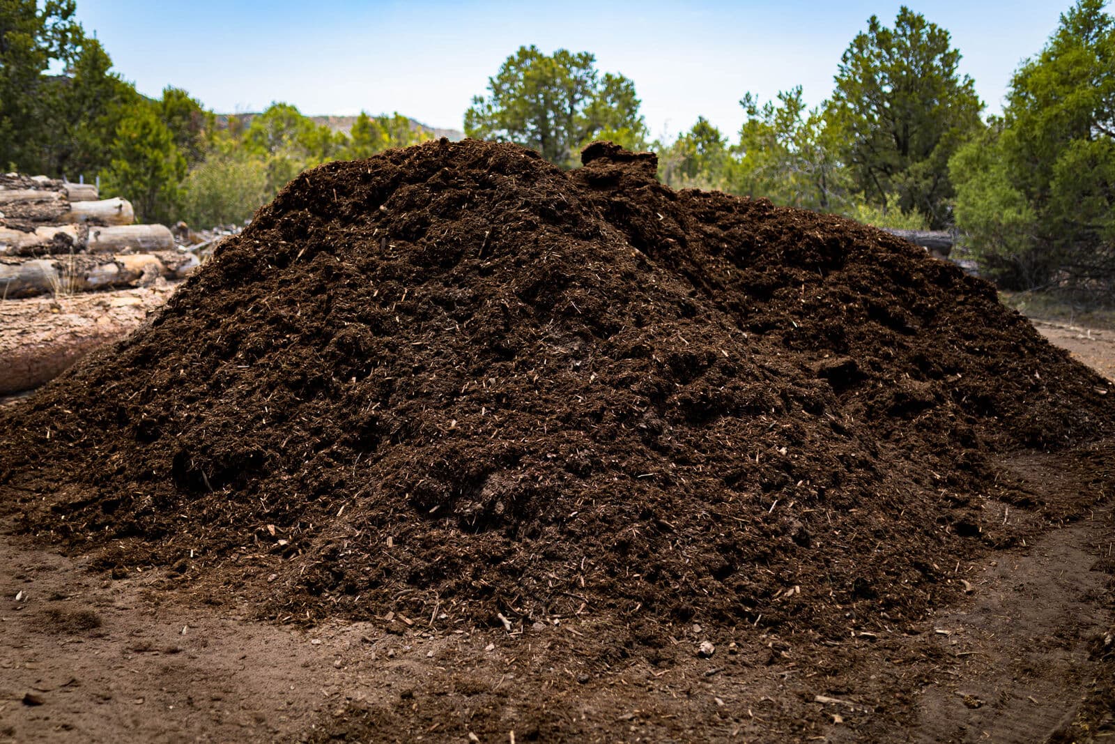 Fresh bulk Western Red Cedar mulch pile with cedar logs in the LandEx Earthworks yard, ready for delivery by the cubic yard in Durango, Colorado